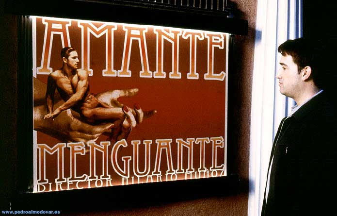 Man looking at movie poster for "AMANTE MENGUANTE." The poster depicts a shrunken man held in a woman's hands.